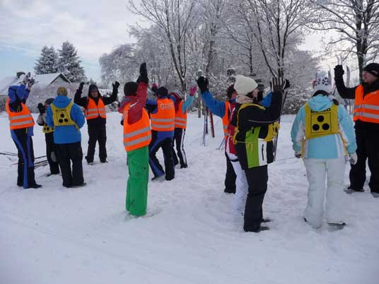 Viele Schüler und Betreuer stehen dick angezogen mit Handschuhen und Mützen an der Loipe im Schnee und wärmen sich mit verschiedenen Armbewegungen auf.