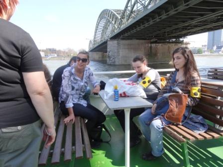 Fahrt mit dem Schiff auf dem Rhein unter der Hohenzollernbrücke. Die Schüler Hazal und Vivian sitzen an einem Tisch mit Frau Czajka.