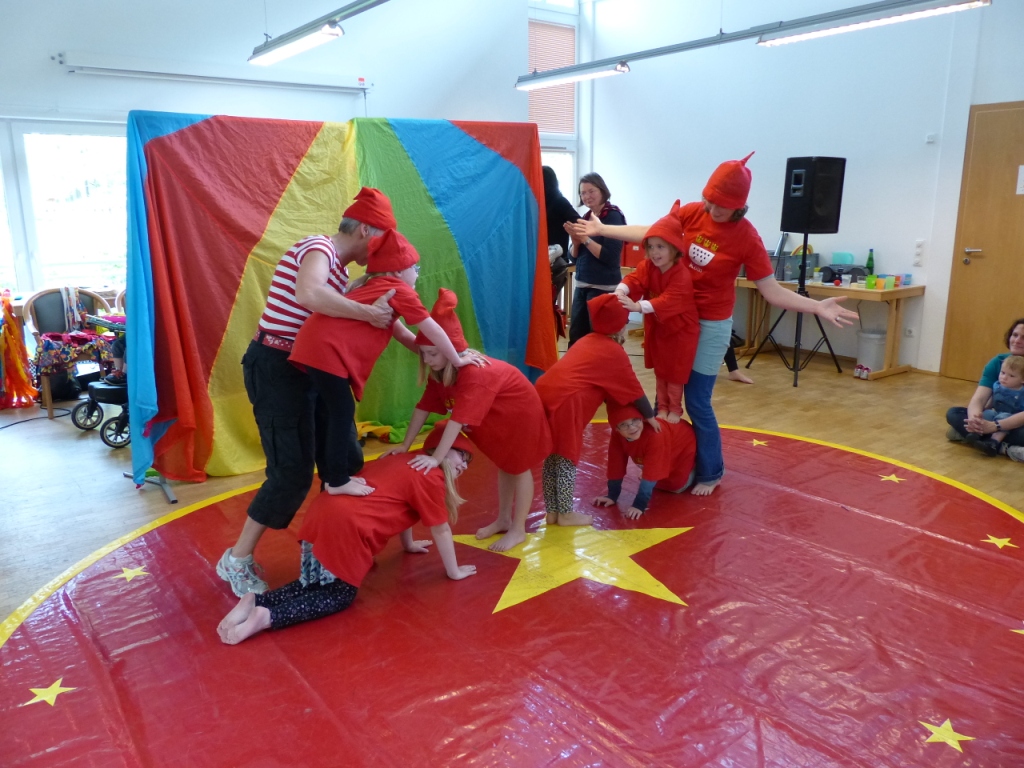 Sechs Kinder machen eine Menschenpyramide auf eine bunten Tuch, das als Zirkusmanege dient.