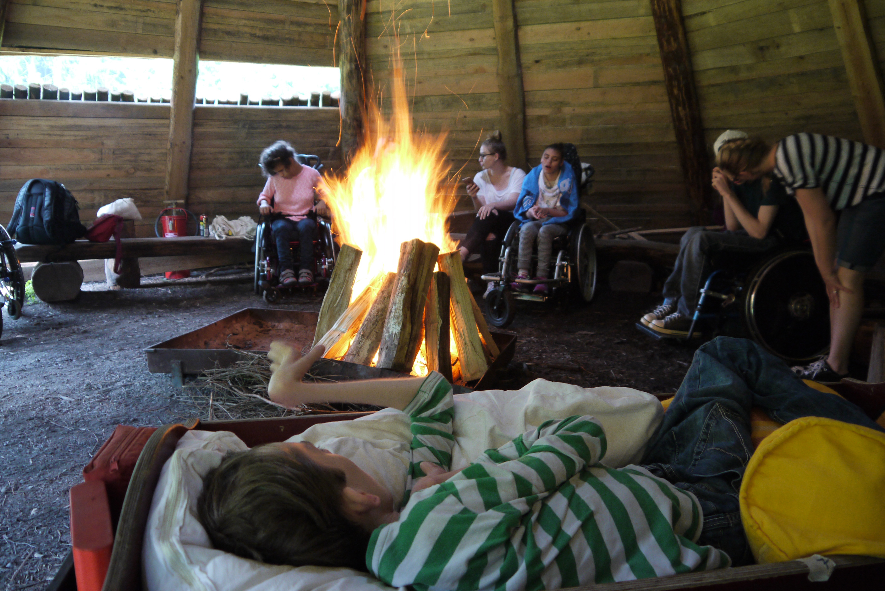 Jugendliche und Betreuer sitzen in der Hütte um das prasselnde Lagerfeuer herum.