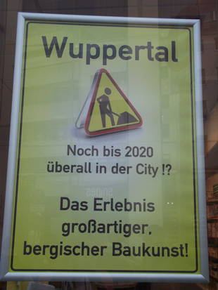 Plakat mit Baustellenschild und Text 'Wuppertal - Noch bis 2020 in der City!? Das Erlebnis großartiger, bergischer Baukunst!'