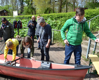 Anton, Eva und Till erkunden ein Kanu auf dem Bootssteg.