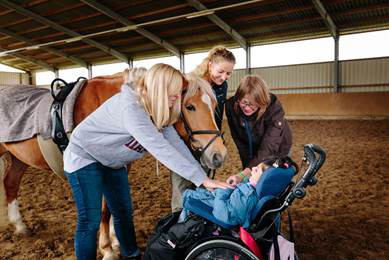 Unterstützt von Lehrern und Therapeuten der LVR-Louis-Braille-Schule streichelt Julia das Pferd und begrüßt es.