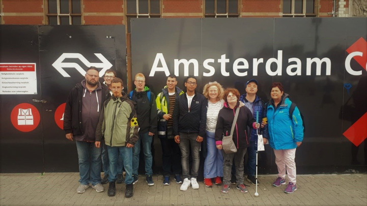 Gruppenbild der Amsterdam-Gruppe vor einem U-Bahnschild mit der Aufschrift 'Amsterdam'