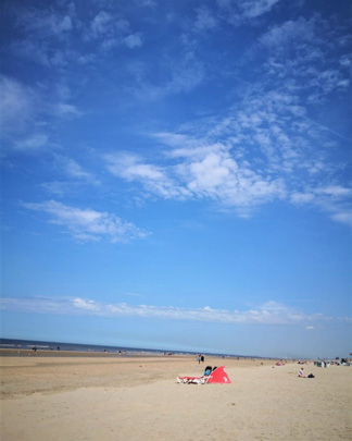 Ein Windschutz steht am Strand unter blauem Himmel