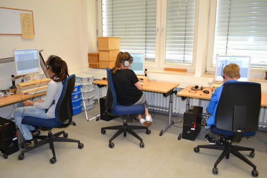 Drei Schüler*innen sitzen am Computer und erforschen das Programm Audacity.