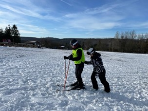Schüler auf Skiern wird vom Guide angeschoben.