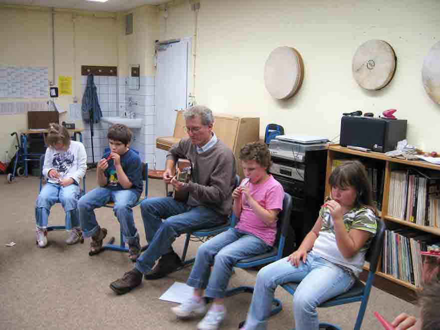 Herr Großnick spielt Gitarre und die Schüler, die neben ihm sitzen, spielen Kazoo.